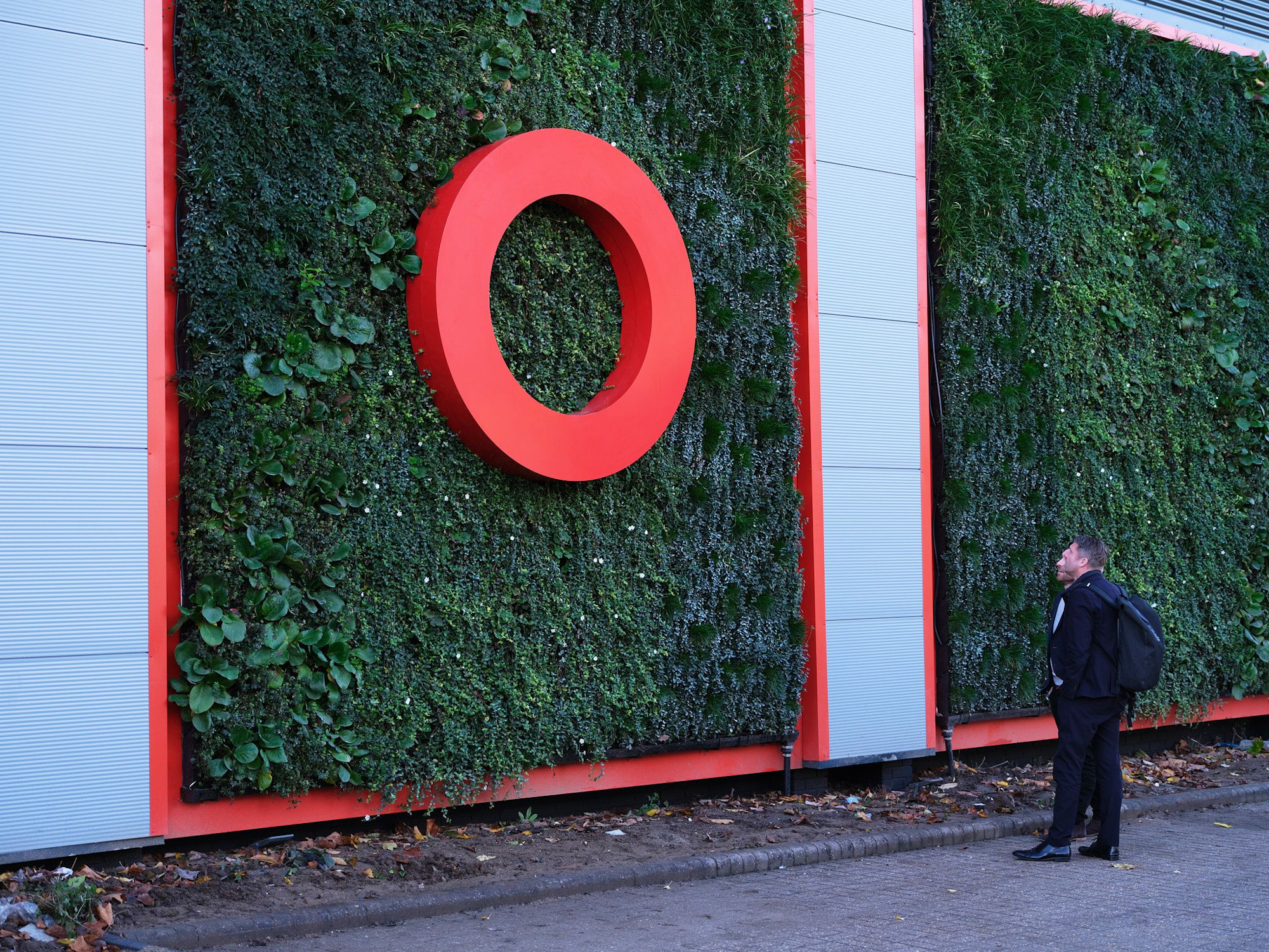 two men looking at the plants in a living wall with red signage