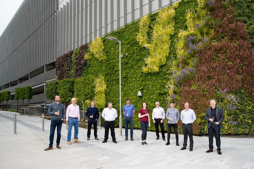 group of people standing in front of a car park with a living wall