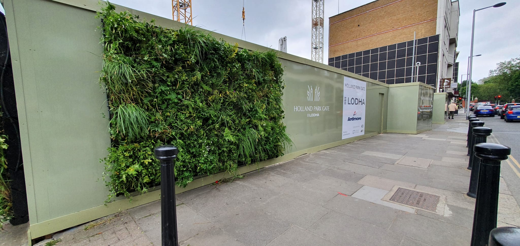 hoarding with green walls around a construction site next to a pavement